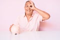 Senior handsome man with gray hair holding piggy bank sitting on the table smiling happy doing ok sign with hand on eye looking Royalty Free Stock Photo