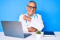 Senior handsome man with gray hair wearing doctor uniform working using computer laptop cheerful with a smile of face pointing Royalty Free Stock Photo