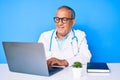 Senior handsome man with gray hair wearing doctor uniform working using computer laptop with a happy and cool smile on face Royalty Free Stock Photo