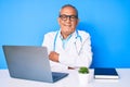 Senior handsome man with gray hair wearing doctor uniform working using computer laptop happy face smiling with crossed arms Royalty Free Stock Photo