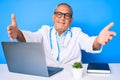 Senior handsome man with gray hair wearing doctor uniform working using computer laptop looking at the camera smiling with open Royalty Free Stock Photo