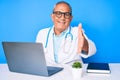 Senior handsome man with gray hair wearing doctor uniform working using computer laptop smiling friendly offering handshake as Royalty Free Stock Photo