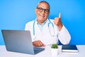 Senior handsome man with gray hair wearing doctor uniform working using computer laptop smiling with happy face looking and Royalty Free Stock Photo