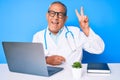 Senior handsome man with gray hair wearing doctor uniform working using computer laptop smiling with happy face winking at the Royalty Free Stock Photo