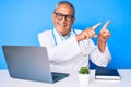 Senior handsome man with gray hair wearing doctor uniform working using computer laptop smiling and looking at the camera pointing Royalty Free Stock Photo