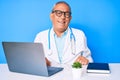 Senior handsome man with gray hair wearing doctor uniform working using computer laptop winking looking at the camera with sexy Royalty Free Stock Photo