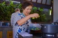 Senior happy and beautiful retired Asian Japanese couple cooking together at home kitchen enjoying preparing meal relaxed in aged