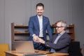 Senior happy businessman in suit with colleague discussing over laptop and making handshake in office Royalty Free Stock Photo