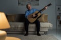 Senior happy man plays acoustic guitar while sitting on sofa Royalty Free Stock Photo