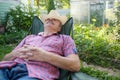 Senior hispanic man in hat sitting leaning back on chair sleeping in outdoor summer flower garden Royalty Free Stock Photo