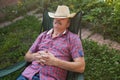 Senior hispanic man in hat sitting leaning back on chair sleeping in outdoor summer flower garden Royalty Free Stock Photo