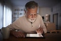 Senior Hispanic man sits at table using stylus and tablet computer at home in the evening, close up