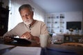 Senior Hispanic man sitting at his dining table reading an e book at home in the evening, close up Royalty Free Stock Photo