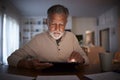 Senior Hispanic man sitting at a table reading an e book at home in the evening, close up Royalty Free Stock Photo