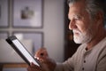 Senior Hispanic man sitting at a table using a tablet computer  in the evening, close up, side view Royalty Free Stock Photo