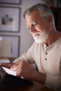 Senior Hispanic man sitting at a table using a tablet computer in the evening, close up, vertical Royalty Free Stock Photo