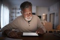 Senior Hispanic man sitting at a table using a tablet computer at home in the evening, close up Royalty Free Stock Photo