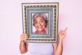 Senior hispanic woman holding empty frame smiling happy pointing with hand and finger to the side Royalty Free Stock Photo