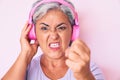 Senior hispanic woman listening to music using headphones annoyed and frustrated shouting with anger, yelling crazy with anger and