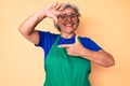 Senior hispanic woman wearing apron and glasses smiling making frame with hands and fingers with happy face Royalty Free Stock Photo