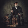 Senior hunter with a english setter and shotgun in a traditional shooting clothing, sitting on a dark background. Royalty Free Stock Photo