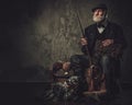 Senior hunter with a english setter and shotgun in a traditional shooting clothing, sitting on a dark background. Royalty Free Stock Photo