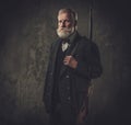 Senior hunter with a shotgun in a traditional shooting clothing, posing on a dark background. Royalty Free Stock Photo