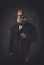 Senior hunter with a shotgun in a traditional shooting clothing, posing on a dark background. Royalty Free Stock Photo