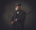 Senior hunter with a shotgun in a traditional shooting clothing, posing on a dark background. Royalty Free Stock Photo