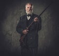 Senior hunter with a shotgun in a traditional shooting clothing, posing on a dark background. Royalty Free Stock Photo