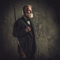 Senior hunter with a shotgun in a traditional shooting clothing, posing on a dark background.