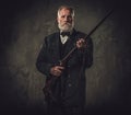 Senior hunter with a shotgun in a traditional shooting clothing, posing on a dark background.