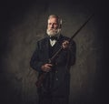 Senior hunter with a shotgun in a traditional shooting clothing, posing on a dark background.