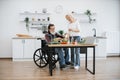 Senior husband in wheelchair and wife mixing chopped vegetables in bowl.