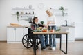 Senior husband in wheelchair and wife mixing chopped vegetables in bowl.