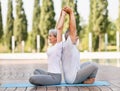 Senior husband and wife performing couple yoga outside in city park sitting on mat in lotus position Royalty Free Stock Photo