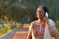 Senior Indian woman laughing and speaking on mobile smart phone in a park wearing off white salwar kamiz. Concept - Digital Royalty Free Stock Photo