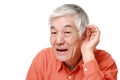 Senior Japanese man with hand behind ear listening closely