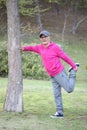 Senior Japanese man wearing pink parka doing standing front thigh stretch