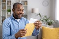 Senior joyful man sitting on sofa at home, satisfied smiling african american man reading mail message holding letter Royalty Free Stock Photo