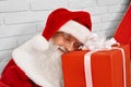Senior Santa Claus sleeping on red gift box in white studio