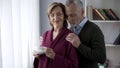 Senior lady drinking tea by window, husband hugging her from behind, trust Royalty Free Stock Photo