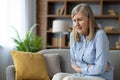 Senior lady holding stomach with both arms while suffering from severe spasms and abdominal pain indoors. Frowning woman Royalty Free Stock Photo