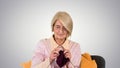 Senior lady knitting sitting on a chair on gradient background. Royalty Free Stock Photo