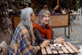 Senior lady laughs spending time with friend at table with candies in street cafe