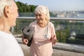 Senior lady with mat and earphones talks to man on footbridge