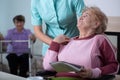 Lady reading a newspaper in common room of professional nursing home with helpful social worker supporting her Royalty Free Stock Photo