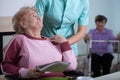 Senior reading a newspaper in common room of professional nursing home with helpful social worker supporting her Royalty Free Stock Photo