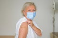 Senior lady wearing a face mask showing her arm to prove she has been vaccinated