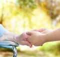 Senior lady in wheel chair holding hands with young caretaker Royalty Free Stock Photo